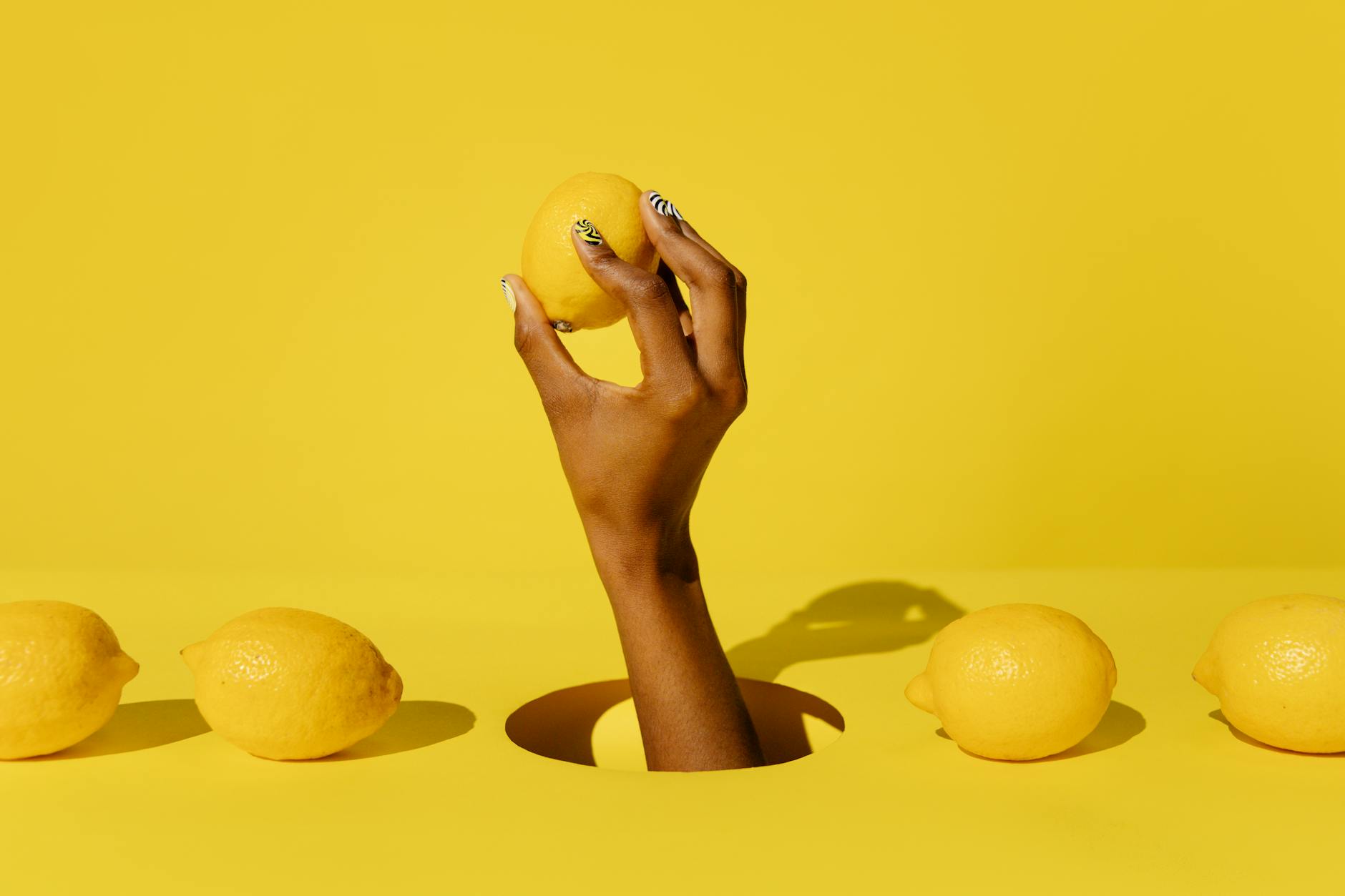 A hand holding a lemon against a bright yellow background, symbolizing fresh, citrusy energy