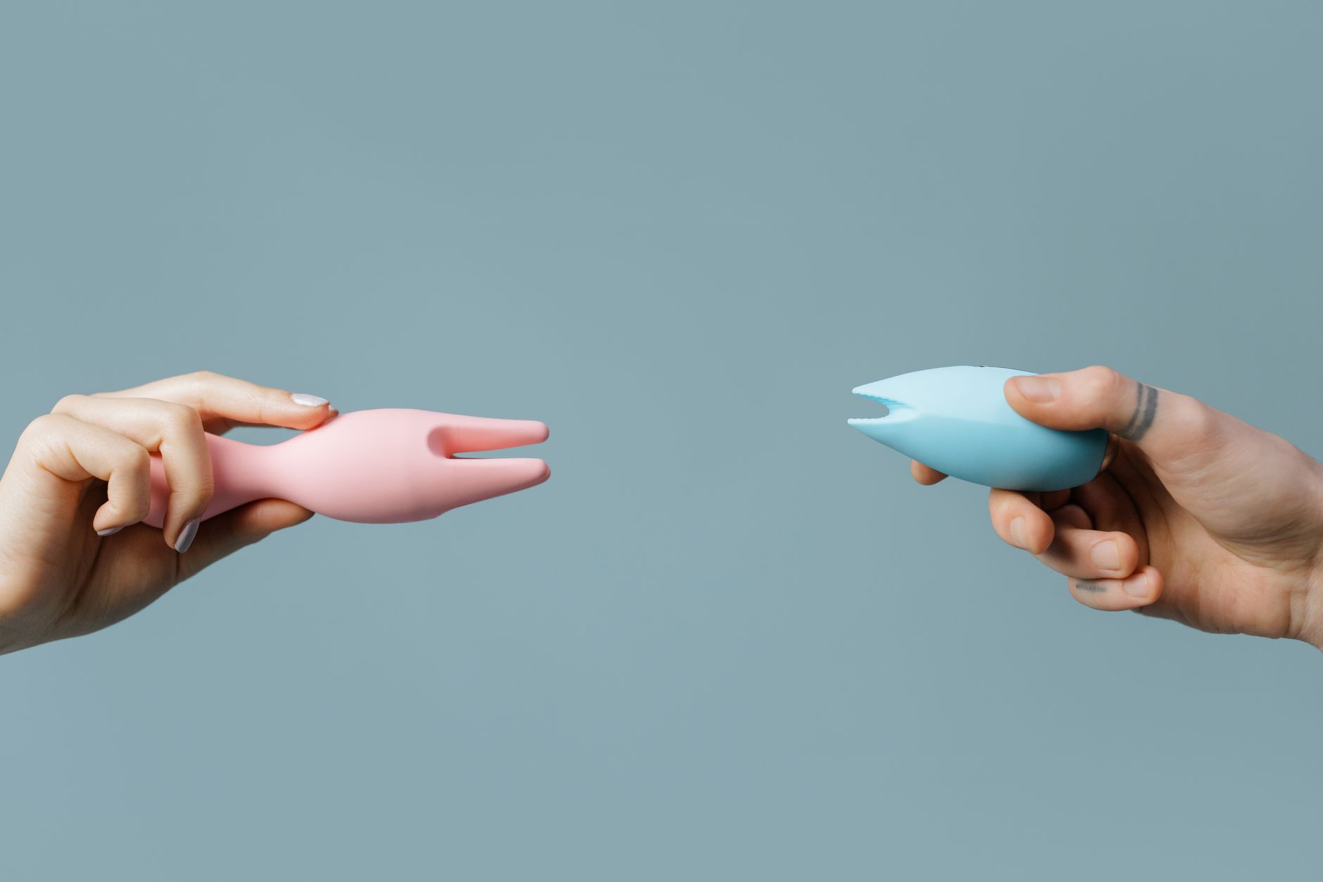 Two hands holding colorful silicone vibrators, representing diverse pleasure preferences and external stimulation options.