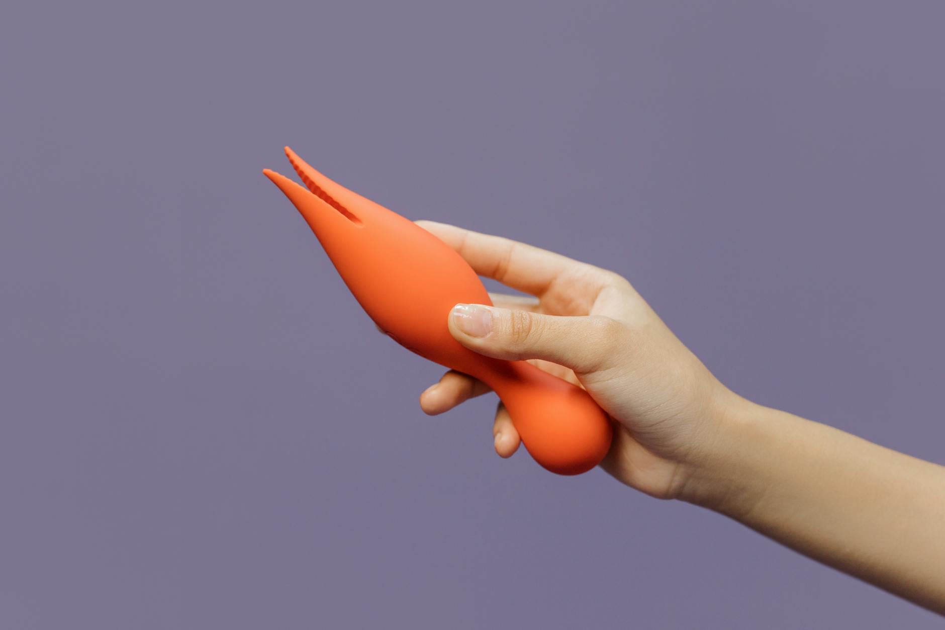 A hand holding a lemon-colored clitoral vibrator against a purple backdrop, representing pleasure and modern wellness